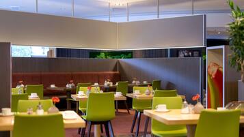 A modern dining area with booths and tables, green chairs, and a television screen.
