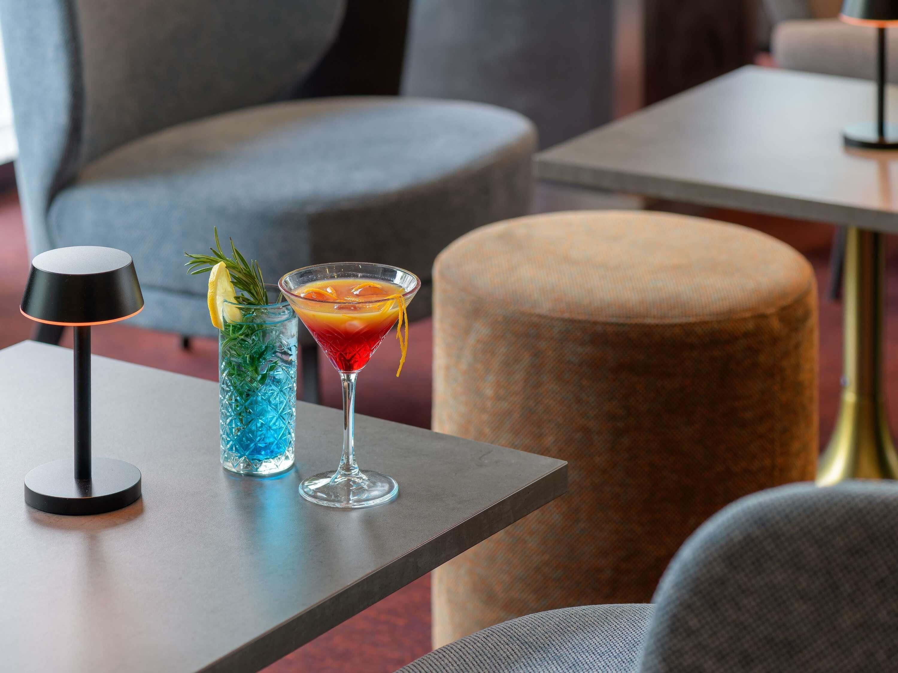 A modern bar area with a cocktail, a blue glass drink, and a black lamp on a table.