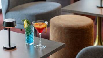 A modern bar area with a cocktail, a blue glass drink, and a black lamp on a table.