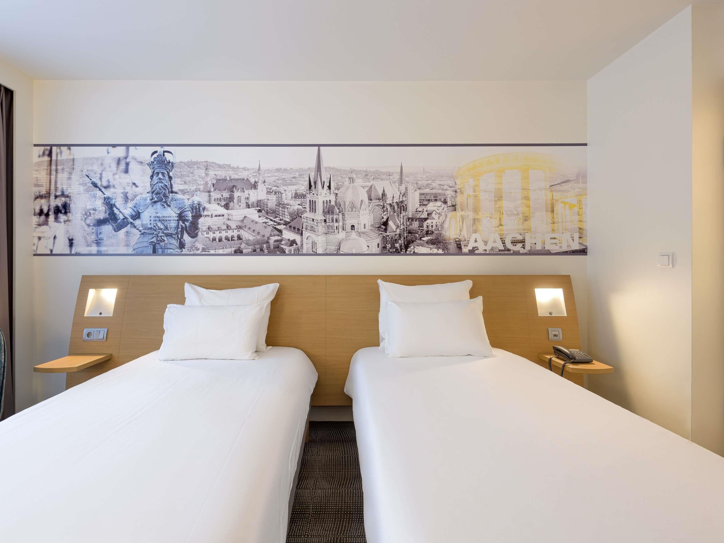 Une chambre d’hôtel avec deux lits, une fresque représentant un paysage urbain, des lampes de chevet et une tête de lit en bois.