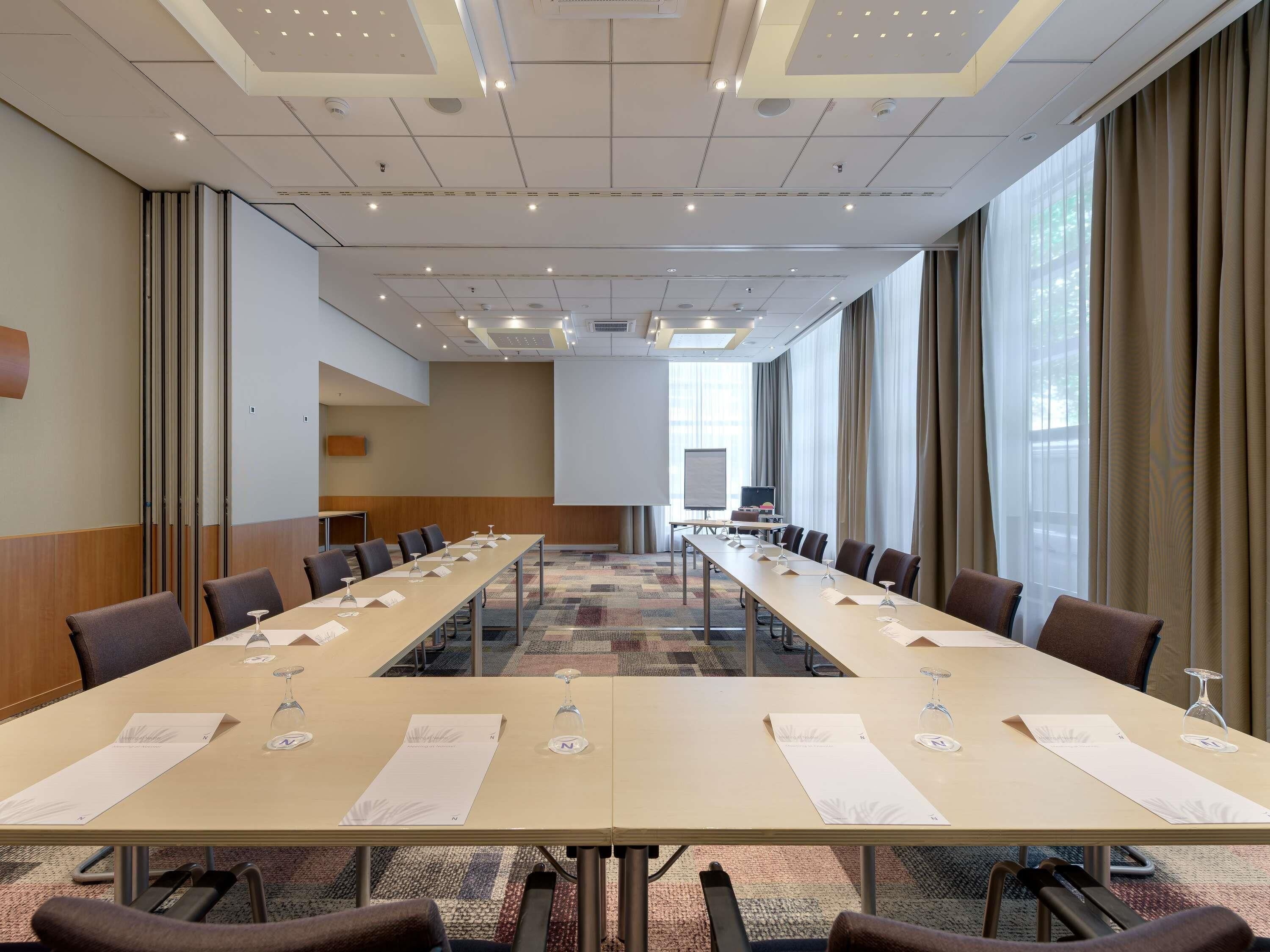 A conference room with a long table, chairs, a projector screen, and a large window.