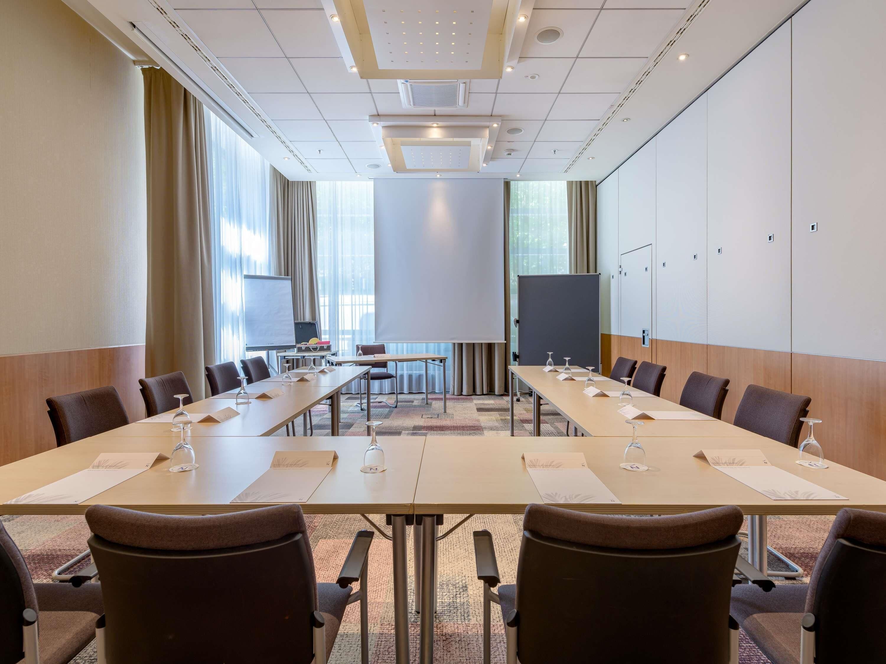A conference room with a long table, chairs, a projector screen, and a whiteboard.