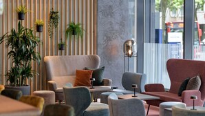 Un'area lounge moderna con varie opzioni di seduta, tra cui divani e poltrone, disposte attorno a un tavolo centrale. Diverse piante in vaso aggiungono un tocco di verde all'ambiente.