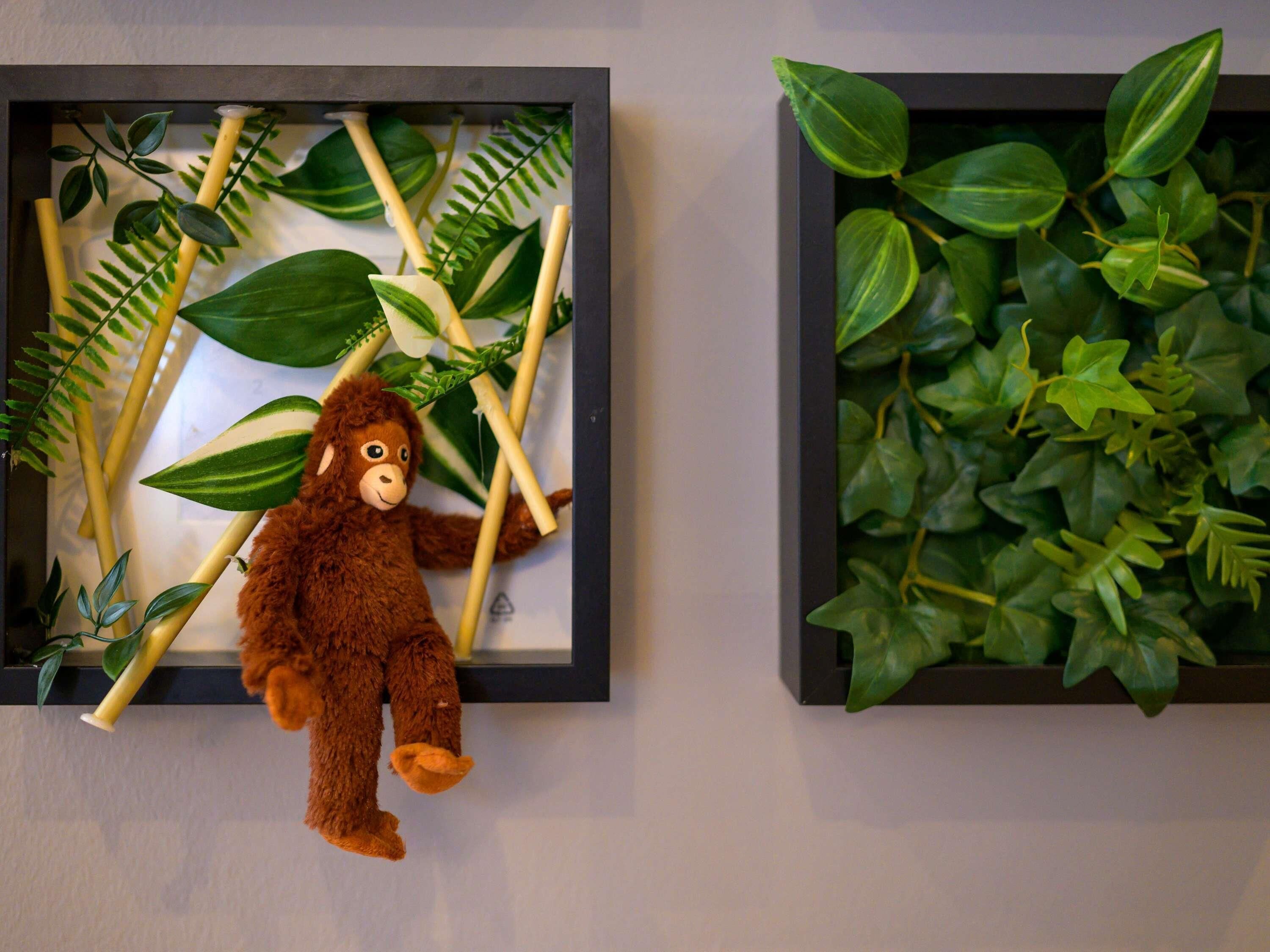 A framed picture with a plush toy and artificial plants.