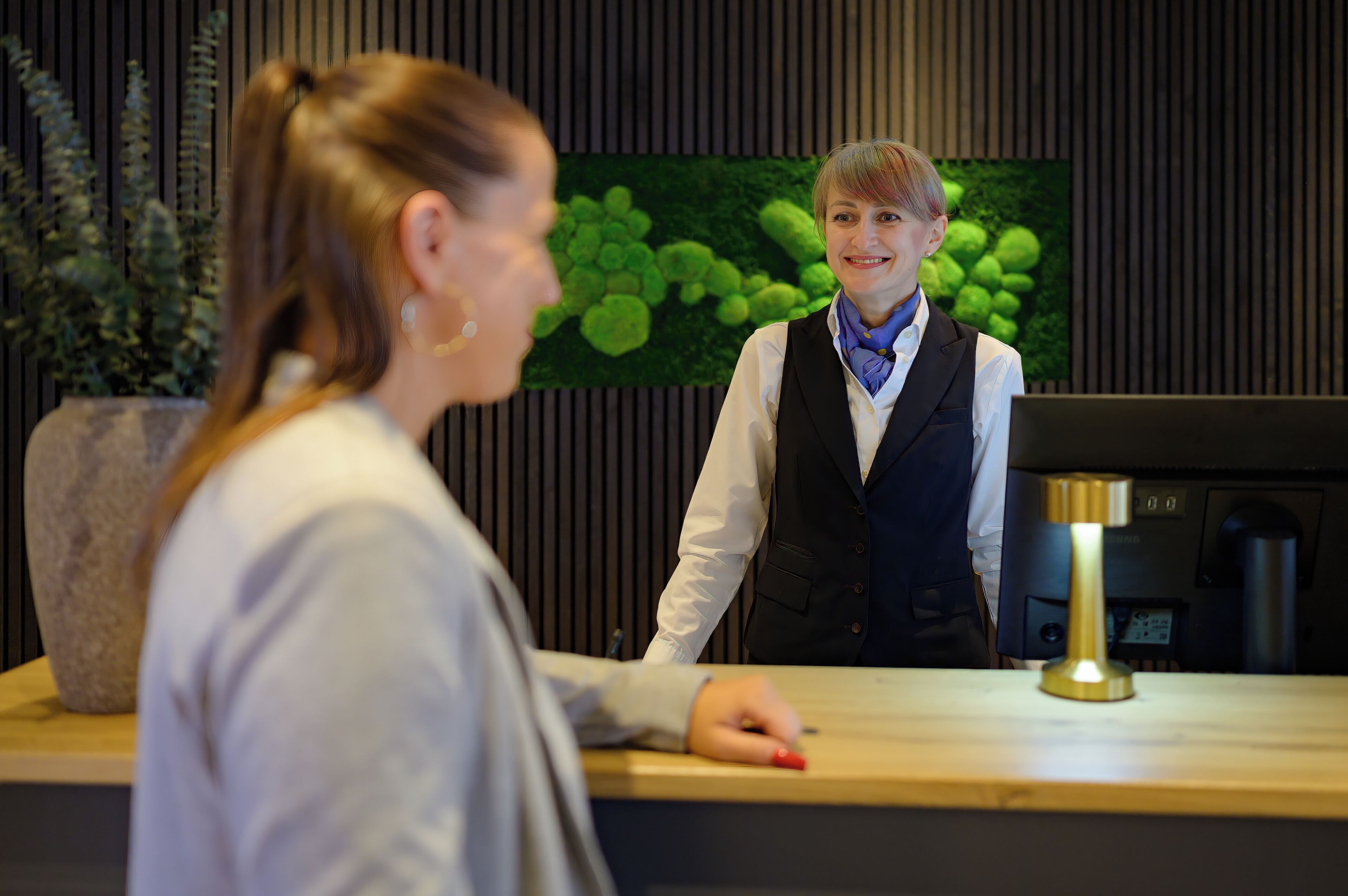 A reception desk with a modern design, a plant, and a digital screen.