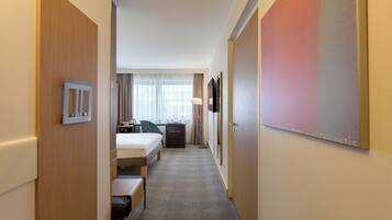 A hotel room with a bed, desk, chair, and a large window with curtains.