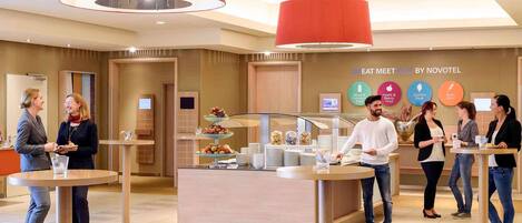 A modern hotel lobby with a buffet area, a reception desk, and a wall displaying the hotel's name and services.