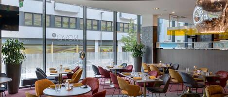 Un interior de restaurante moderno con mesas redondas, sillas cómodas y ventanas amplias.