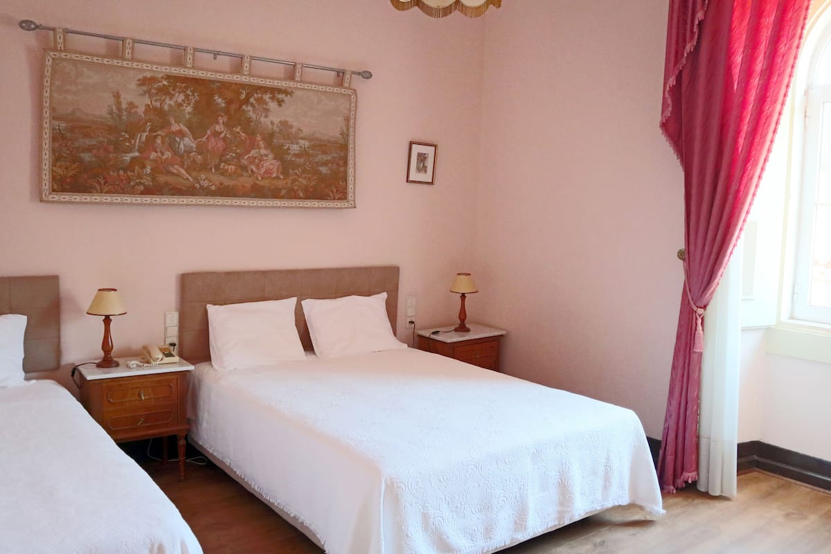 Une chambre avec deux lits, un grand tableau au mur et une fenêtre avec des rideaux.
