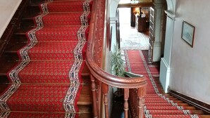 Una imponente escalera con peldaños alfombrados en rojo y barandilla de madera, que conduce a un arco de entrada.