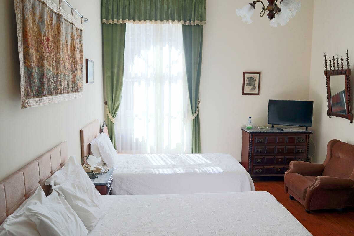 Une chambre d’hôtel avec deux lits, un téléviseur posé sur une commode, une chaise et un tableau accroché au mur.