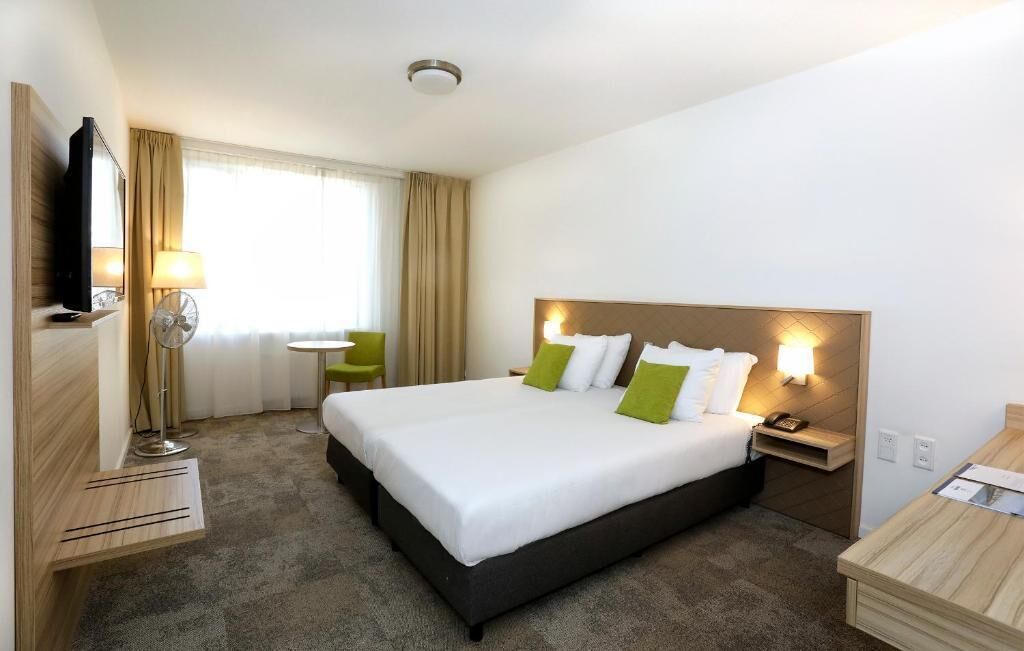 Une chambre d’hôtel avec un grand lit, des tables de chevet, un bureau, une chaise, une télévision et une fenêtre avec des rideaux.