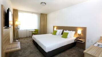 Une chambre d’hôtel avec un grand lit, des tables de chevet, un bureau, une chaise, une télévision et une fenêtre avec des rideaux.
