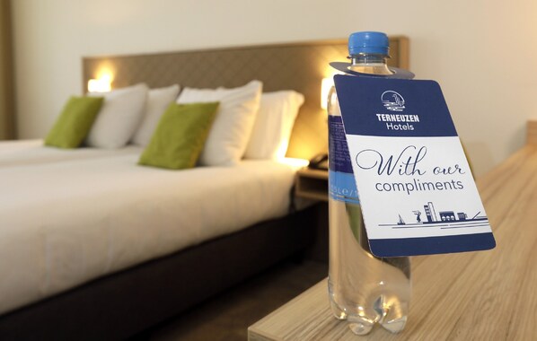 A hotel room with a neatly made bed, a bedside table with a bottle of water and a complimentary card from Tereuzen Hotels.