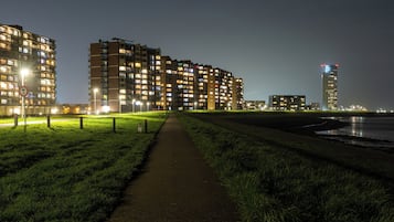A pathway leading to a high-rise building with multiple floors, a beach in the background, and a body of water.