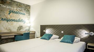 Habitación de hotel con una cama grande, dos almohadas, una mesita de noche, un escritorio y una pared con una cita.