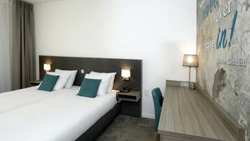 Ein Hotelzimmer mit Bett, Nachttischen, einem Schreibtisch und einem motivierenden Zitat an der Wand.