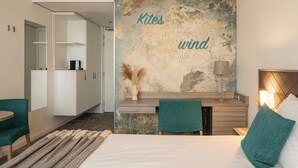 Ein modernes Hotelzimmer mit einem großen Bett, einem Schreibtisch und einer Sitzecke. An der Wand ist ein motivierendes Zitat und es bietet einen Blick auf die Stadt.