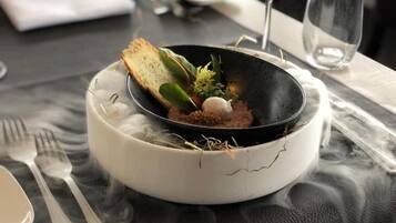 A dining table with a black bowl containing food, a white plate, and a fork.