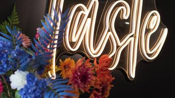 A neon sign spelling "Taste" with a floral arrangement in a copper vase.