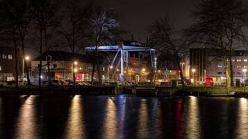 A nighttime view of a riverside area with a bridge, buildings, and parked cars.