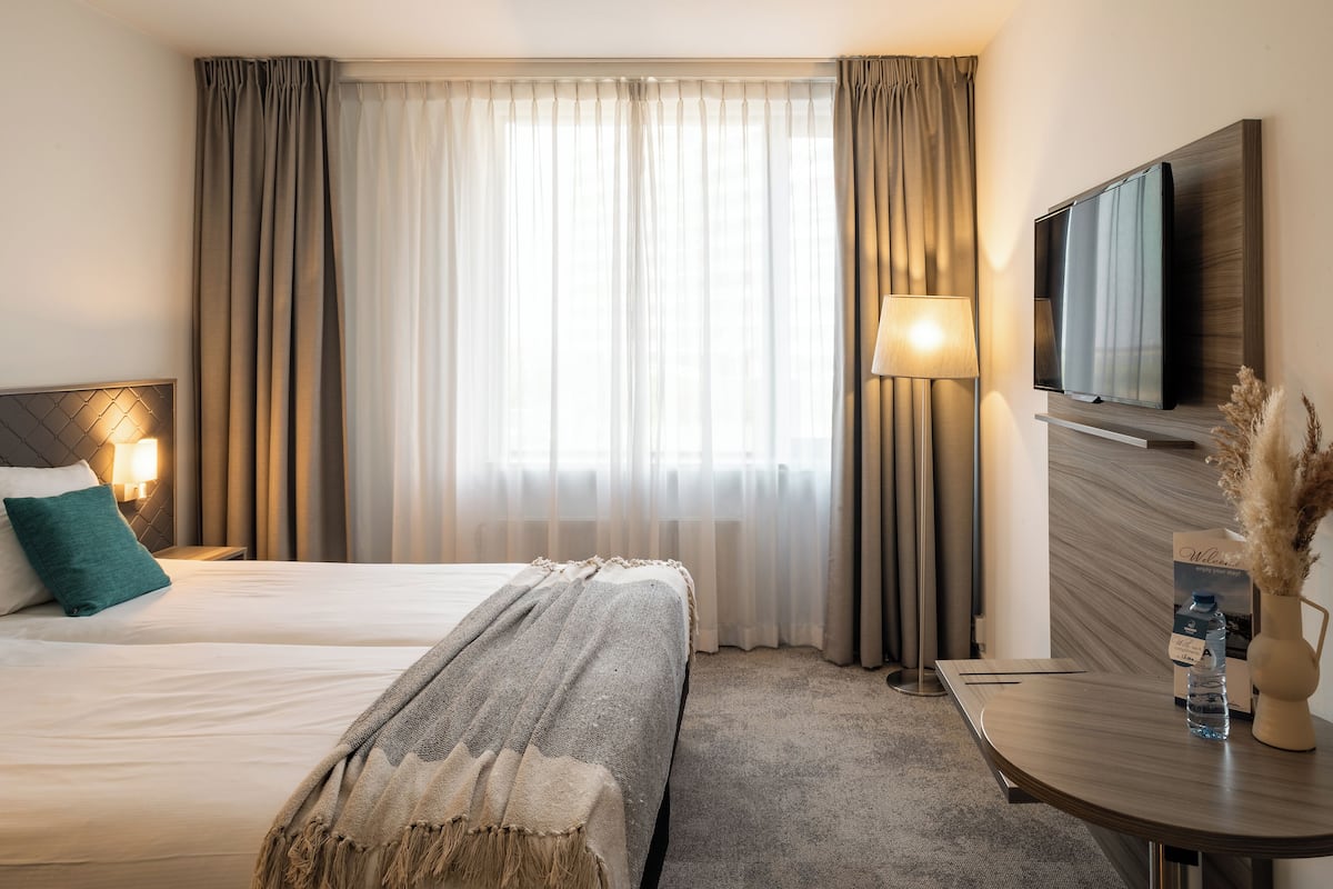 Een hotelkamer met twee bedden, een televisie, een lamp en een tafel met een vaas en een waterfles.