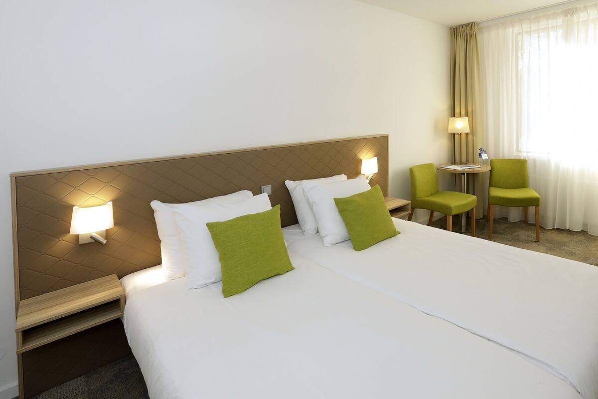 Een hotelkamer met een groot bed, twee nachtkastjes, een lamp, een stoel en een klein tafeltje.