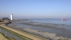 Eine Küstenlandschaft mit einem großen Gewässer, einem roten Schiff und einem hohen Gebäude.
