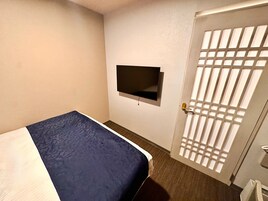 A hotel room with a bed, a television mounted on the wall, and a door with a grid pattern.