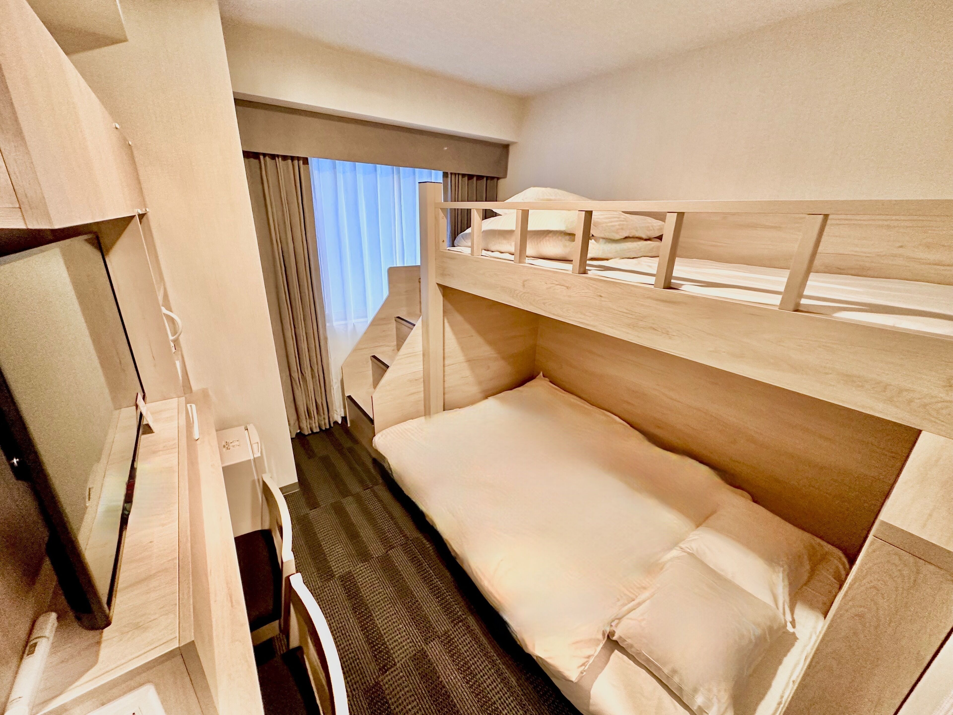 Une chambre d’hôtel avec un lit superposé, une télévision et une fenêtre avec des rideaux.