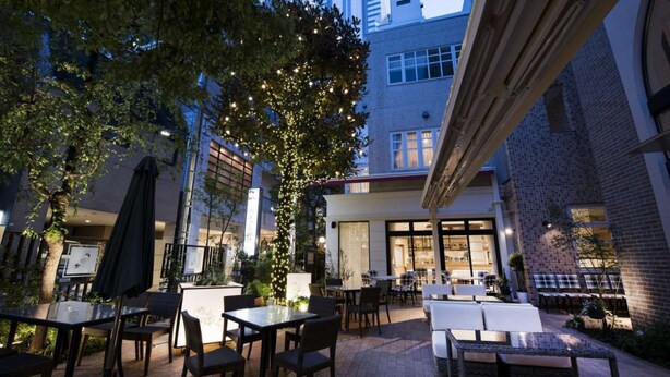 An outdoor patio area with tables and chairs, surrounded by trees and buildings. - Hotel Rose Garden Shinjuku (Tokyo)