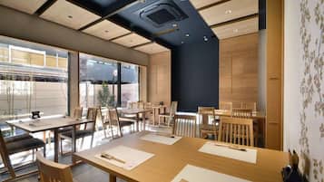 A modern dining area with wooden tables and chairs, large windows, and a dark accent wall.