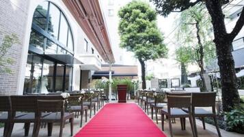 A red carpet leading to a podium, surrounded by tables and chairs, with a building and trees in the background.