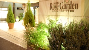The entrance of Hotel Rose Garden with a sign and potted plants. - Hotel Rose Garden Shinjuku (Tokyo)