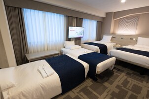 Una habitación de hotel con tres camas, televisor, escritorio y teléfono en la mesita de noche.