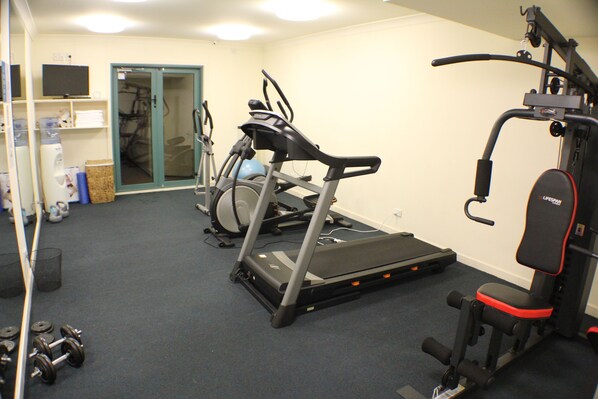 Une salle de sport équipée de divers appareils, notamment des tapis de course, un vélo d’appartement et des appareils de musculation.