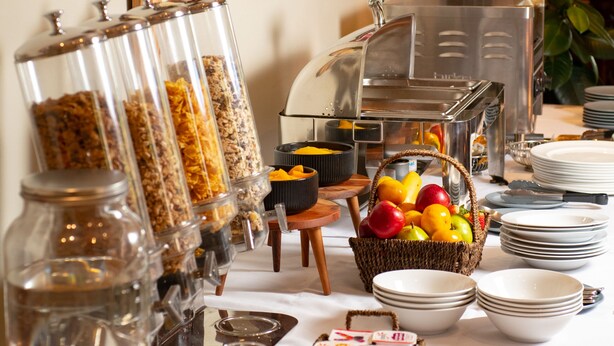 A buffet setup with various food items, a coffee machine, and a fruit basket. - Gateway on Monash Boutique Hotel (Notting Hill)