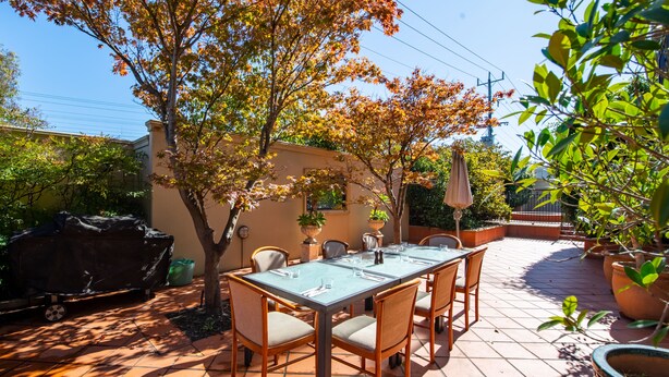 Une terrasse extérieure avec une table rectangulaire mise pour le repas, entourée de chaises.