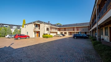 A courtyard with a brick pathway, a building with a balcony, and parked cars.