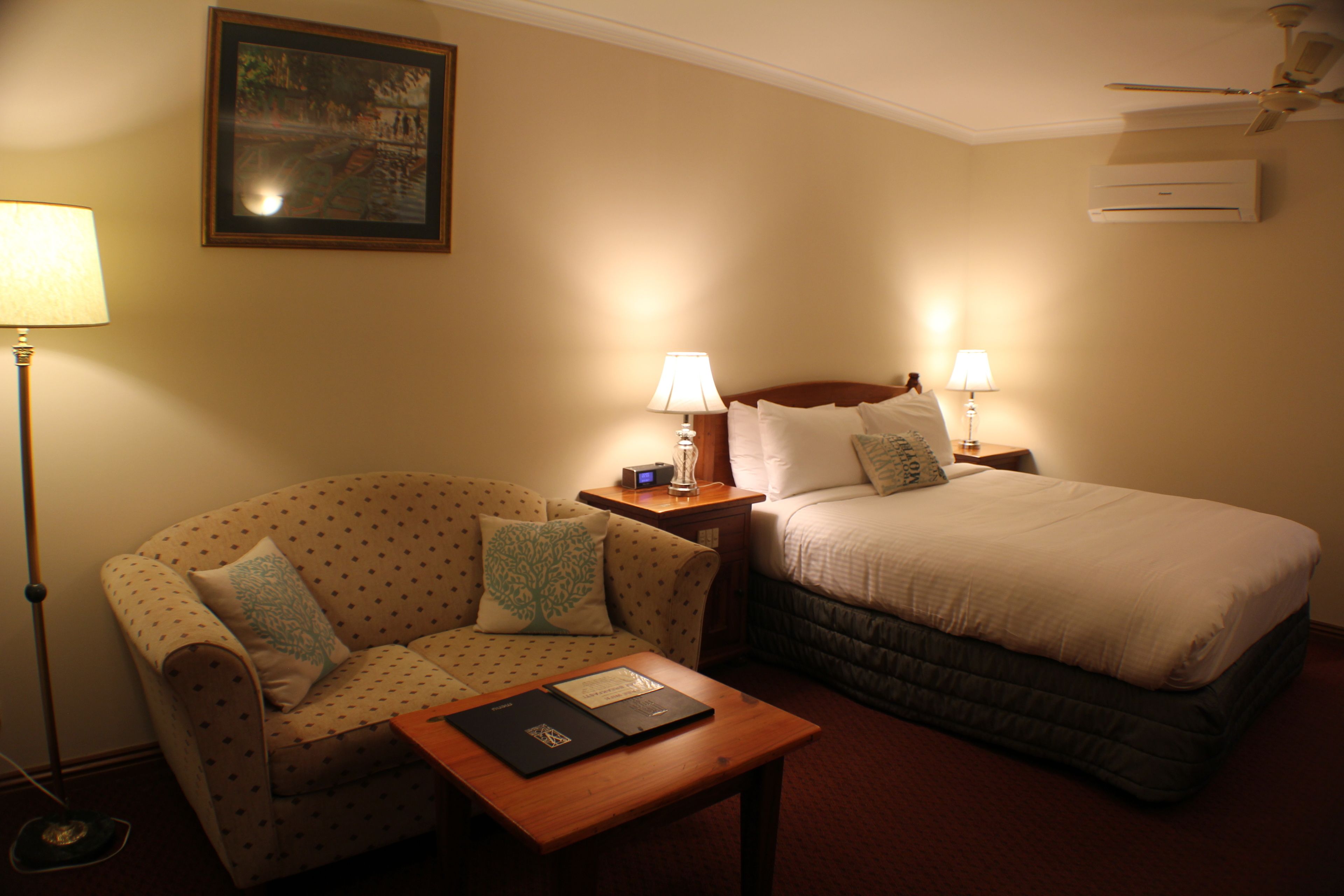 Ein Hotelzimmer mit Bett, Sofa, Nachttisch, Lampe und einem gerahmten Bild an der Wand.