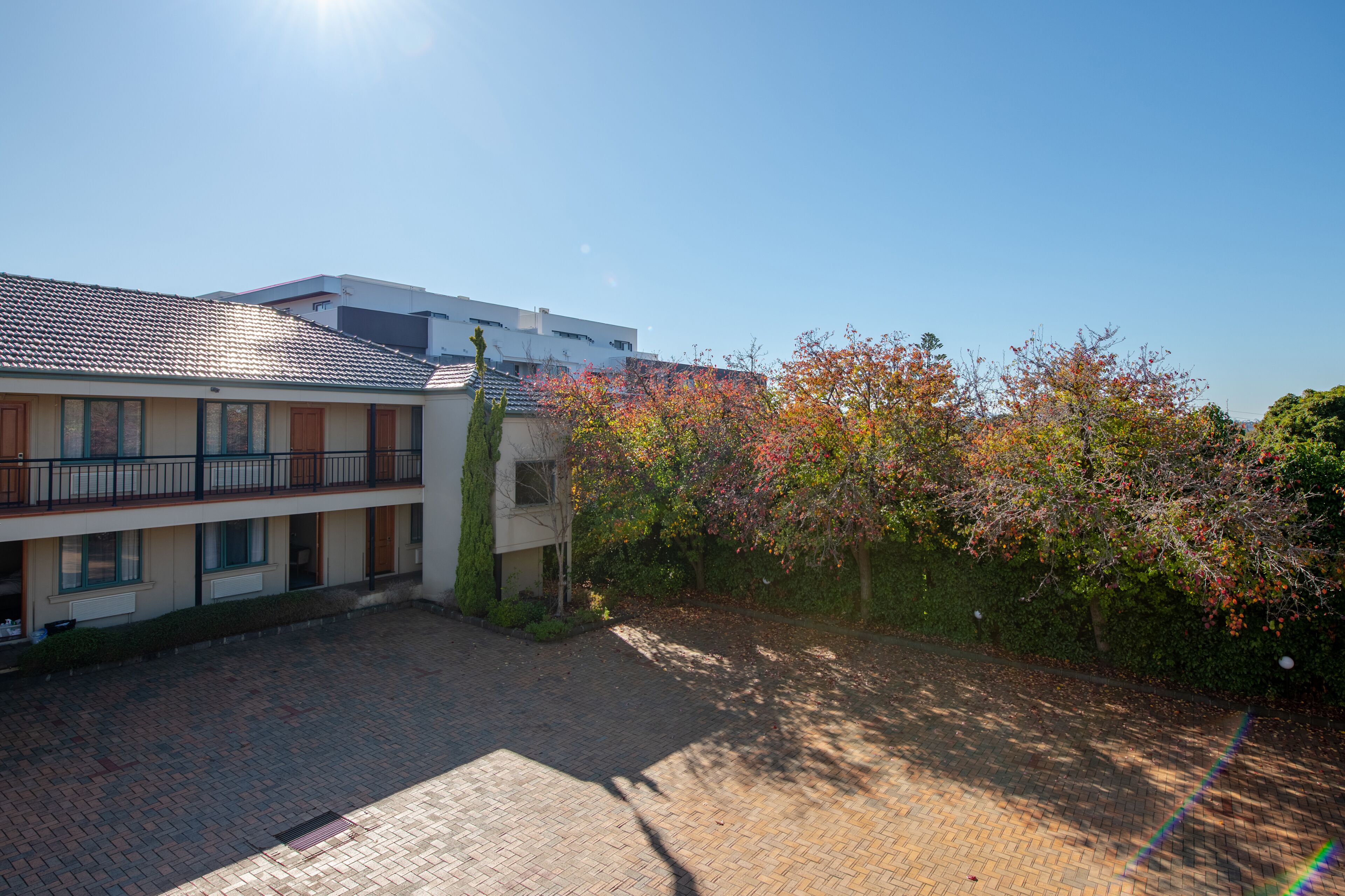 A courtyard with a paved area, a building with a tiled roof, and a tree with autumn foliage.