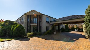 A two-story house with a covered driveway and a large front lawn. - Gateway on Monash Boutique Hotel (Notting Hill)