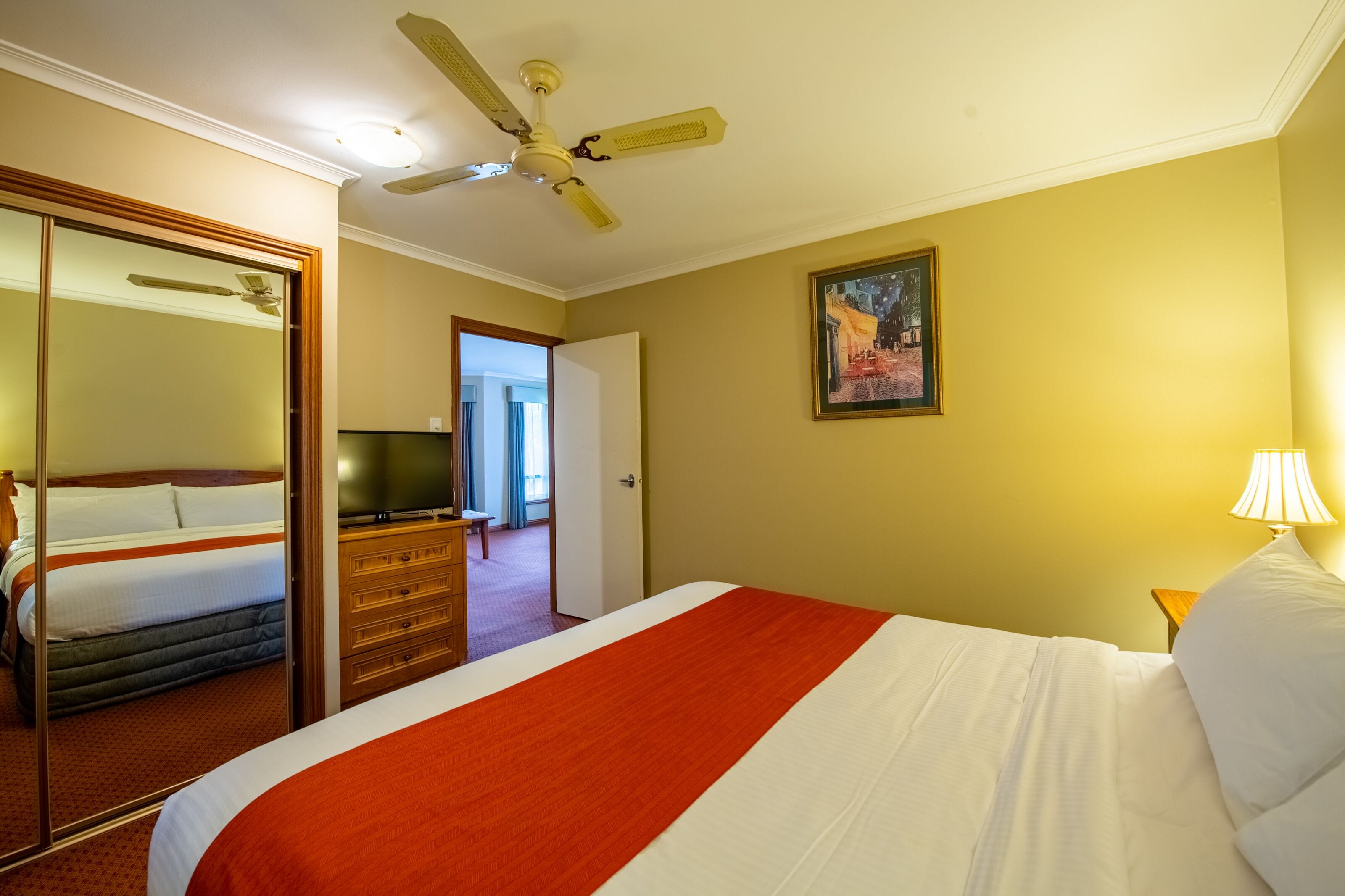 A hotel room with a bed, a television, a dresser, a mirror, and a ceiling fan.