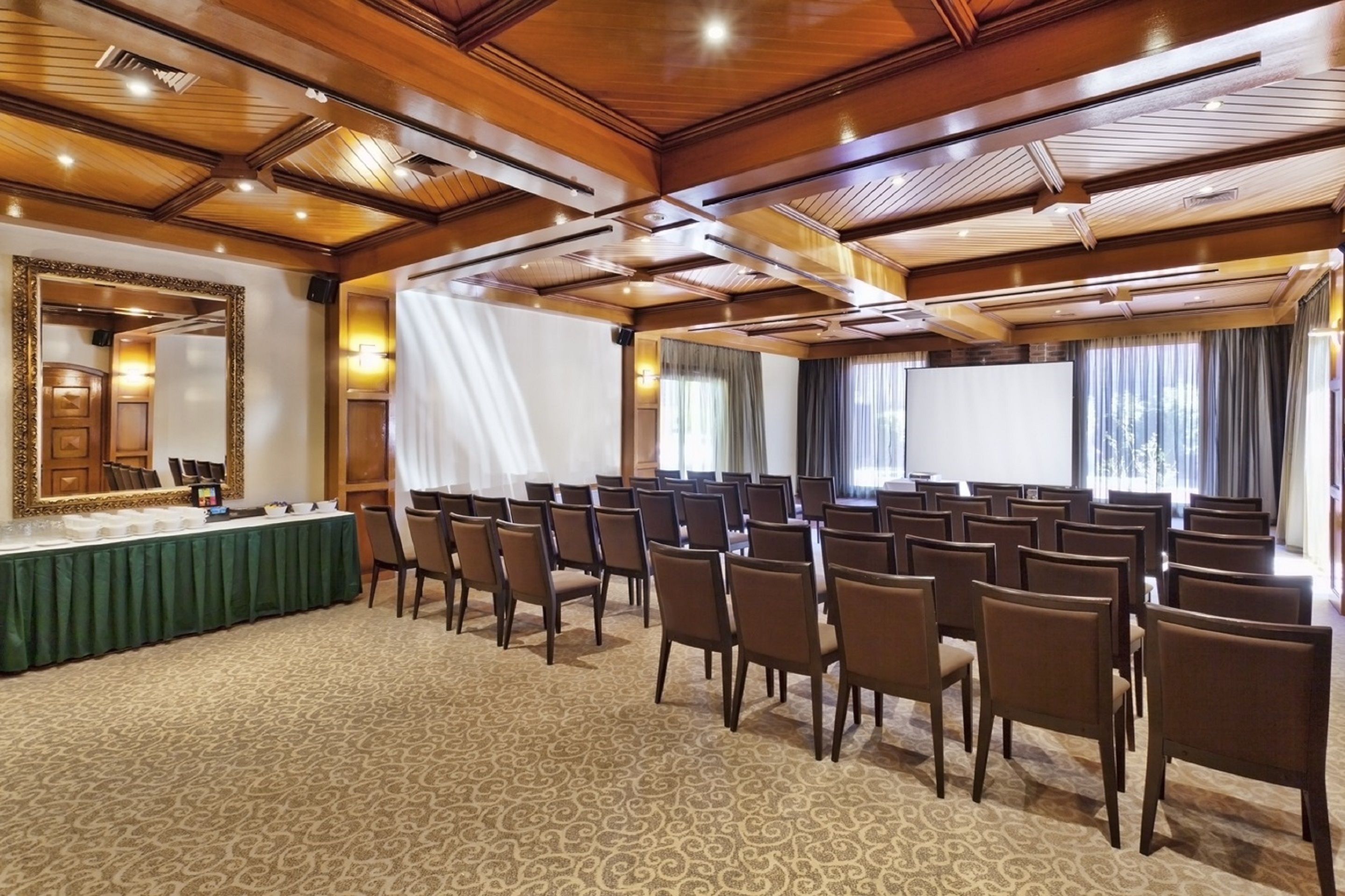 A conference room with rows of chairs, a long table with a green tablecloth, and a large screen.