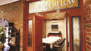 A dining area with a long table set for a meal, a brick wall, and a stained glass sign reading "THE OVERFLOW".