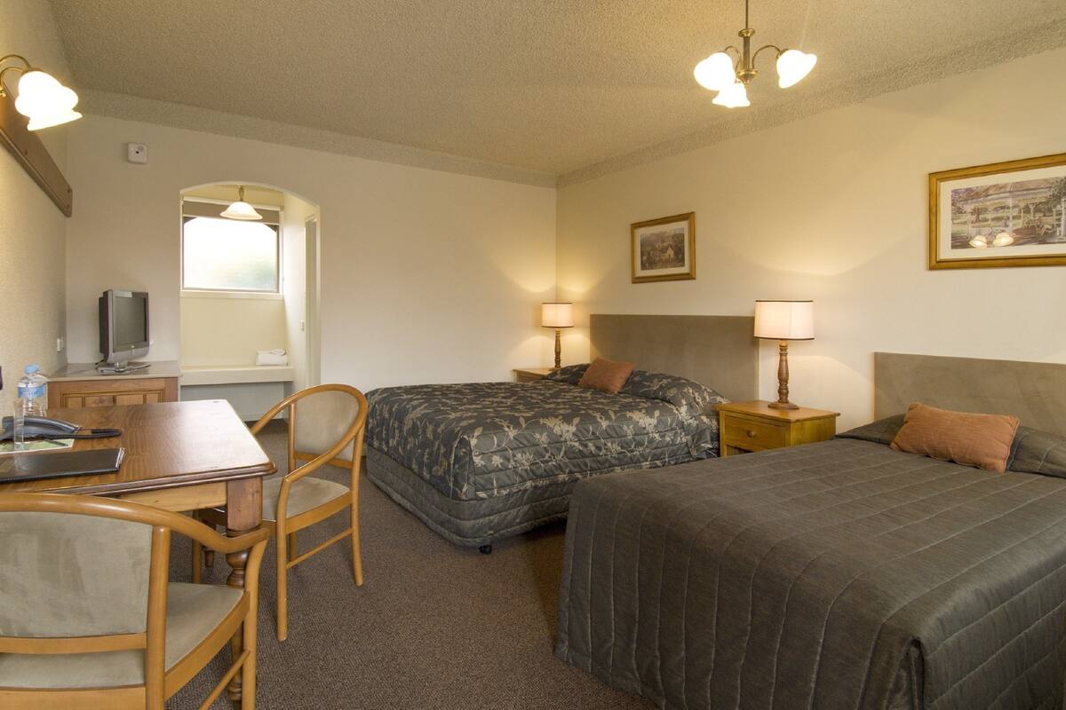 Une chambre d’hôtel avec deux lits, un bureau avec une chaise, une télévision et une fenêtre.