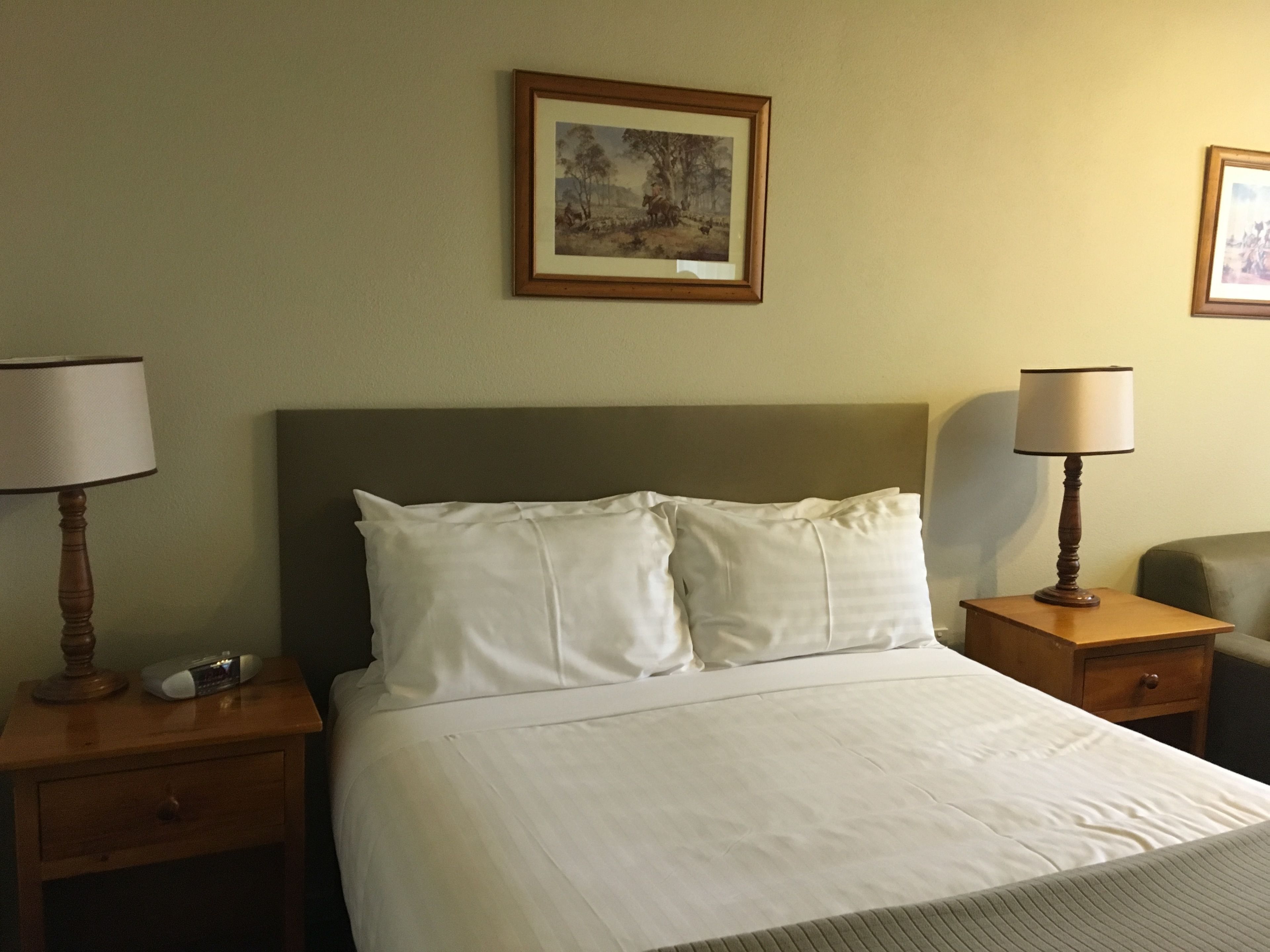 A neatly made bed with white linens, two bedside tables with lamps, and a framed picture on the wall.