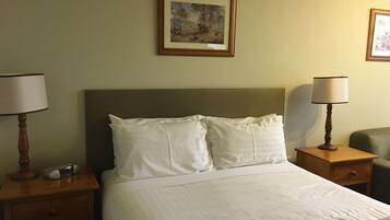 A neatly made bed with white linens, two bedside tables with lamps, and a framed picture on the wall.