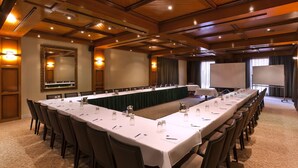 A conference room with a long table, chairs, a projector screen, and a large mirror.