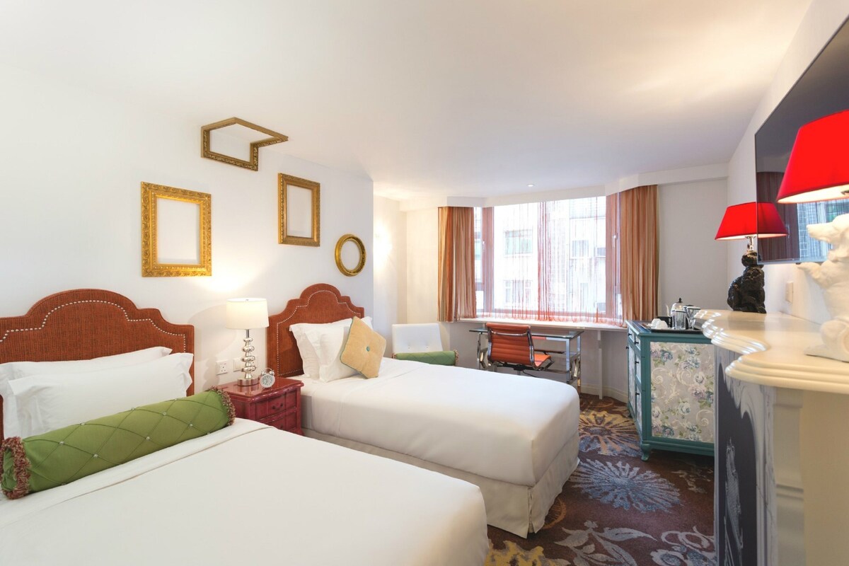 Habitación de hotel con dos camas, un escritorio, una silla, un aparador y una ventana con cortinas.